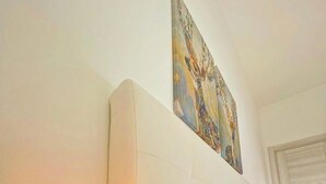 A bedroom with a bed, a wall-mounted painting, and a table lamp.