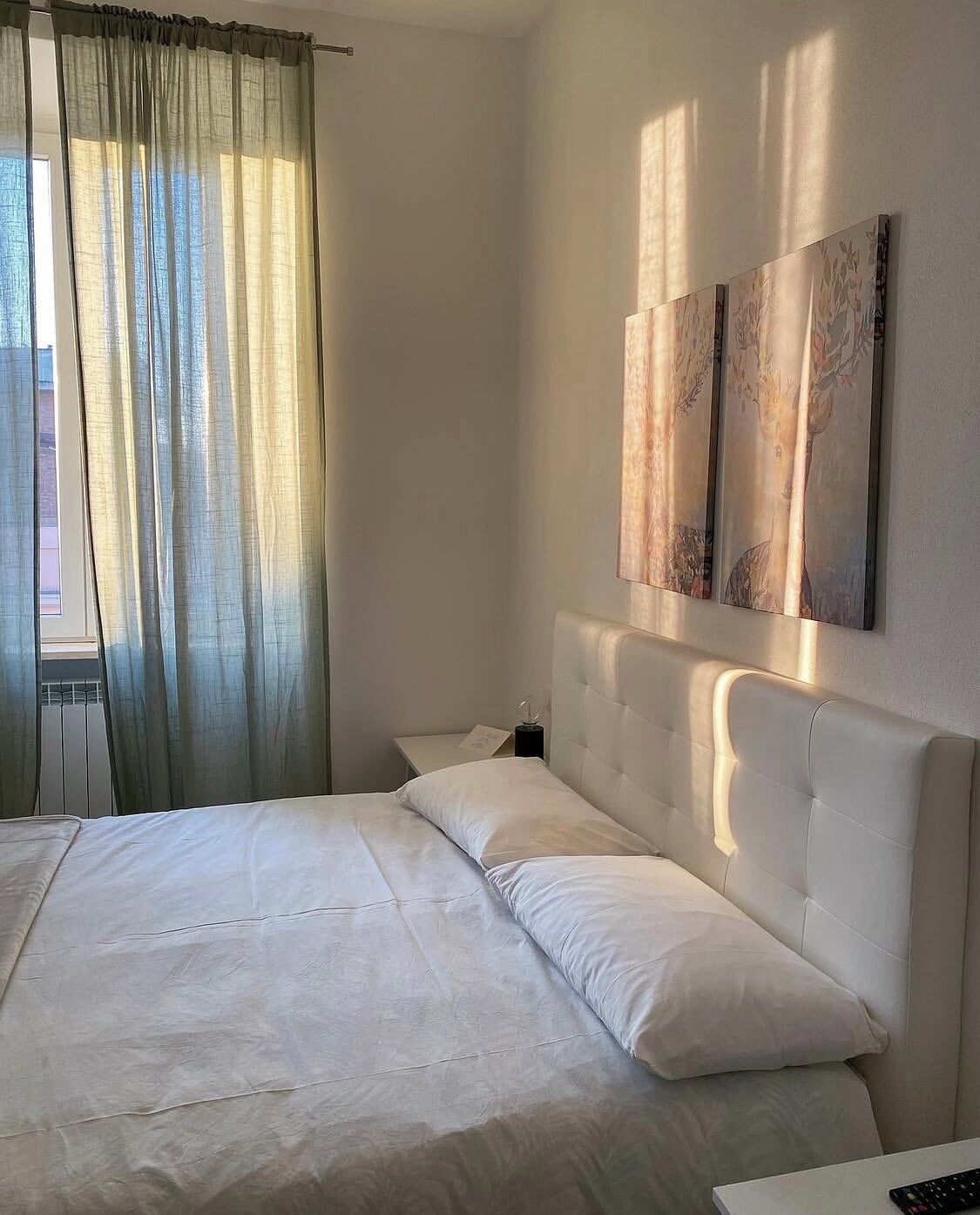 Ein Hotelzimmer mit einem Bett, einem Nachttisch, einer Lampe und Kunstwerken an der Wand.