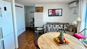 Eine moderne Küche mit weißen Geräten, einem Esstisch mit Obst, einem Sofa und einem kleinen Beistelltisch.