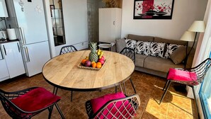 Ein gemütlicher Wohnbereich mit einem runden Holztisch, zwei Stühlen, einer Couch und einer Küchenzeile.