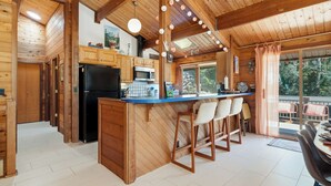 A wooden cabin with a kitchen featuring a black refrigerator, wooden cabinets, a blue countertop, and a bar area with stools. - Lodge style 5 bedroom, 2 kitchens, large deck, outdoor firepit, 1 dog ok (Manzanita)