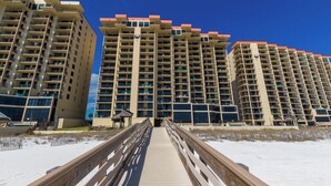 A boardwalk leading to high-rise buildings with balconies, a sandy beach, and a clear blue sky. - Phoenix II 2065 by Liquid Life (Orange Beach)