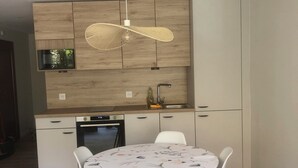 Une cuisine moderne avec des meubles en bois, un four à micro-ondes et un évier. On y trouve une table à manger avec des chaises et un luminaire suspendu.