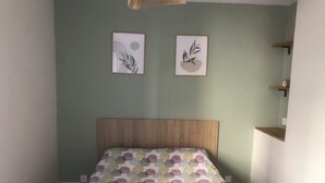 Une chambre à coucher avec une tête de lit en bois, une couvre-lit à pois, deux œuvres d’art encadrées accrochées au mur et une petite étagère sur laquelle se trouve une horloge.