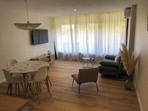 Ein modernes Wohnzimmer mit Essbereich, einem flachbildfernseher an der Wand, einer Couch und einem kleinen Beistelltisch.