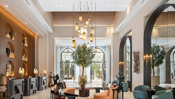 Eine großzügige Lobby mit einer zentralen Sitzgruppe, einem großen Baum und einer Rezeption.
