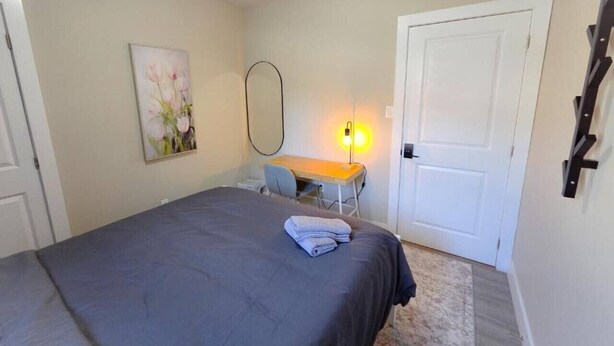 Ein Schlafzimmer mit einem Bett, einem Schreibtisch, einem Stuhl, einem Bild und einer Tür.