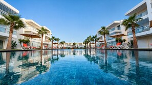 En swimmingpool med liggestole og palmer, omgivet af moderne bygninger.