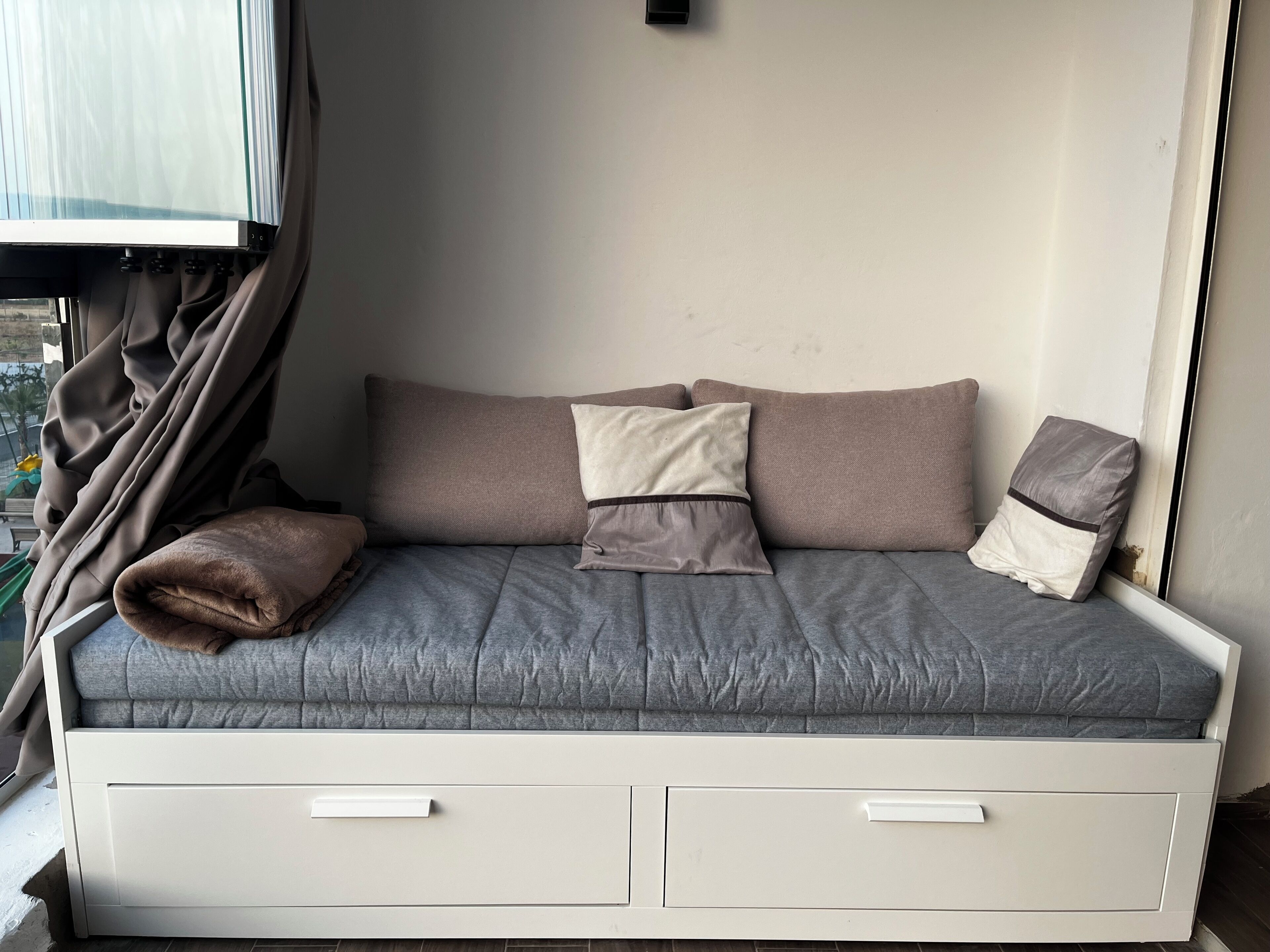 A bed with a grey mattress, two pillows, and a blanket.