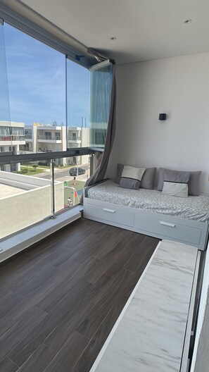 A modern bedroom with a bed, a large window, and a view of the street. - Le Ramo - Ramoflores Residence (Sidi Rahal)
