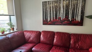 En röd lädersoffa i ett rum med en stor tavla på väggen som föreställer en skog.