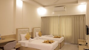 A hotel room with two beds, a desk, a chair, a TV, and an air conditioning unit.