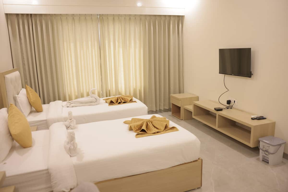 A hotel room with two beds, a TV mounted on the wall, and a small table with a trash bin.