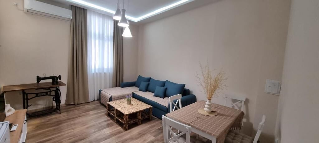 A living room with a sofa, a coffee table, a dining table, and a sewing machine.