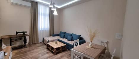 A living room with a sofa, a coffee table, a dining table, and a sewing machine.