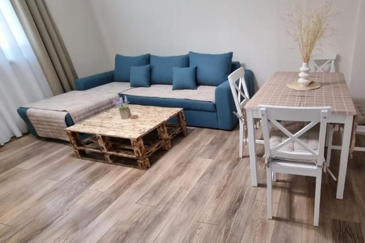 Una habitación con un sofá, una mesa de centro, una mesa de comedor con sillas y un florero con plantas secas.