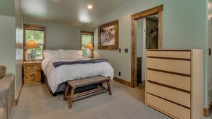 Een slaapkamer met een bed, nachtkastjes, een houten bankje, een kaptafel en een deur naar een badkamer.