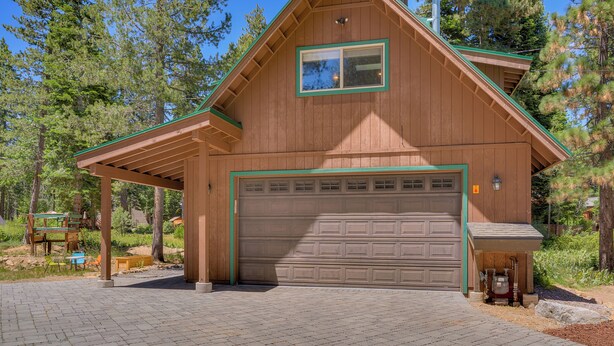 Een houten chalet met garage, overdekte veranda en uitzicht op het omliggende bos.