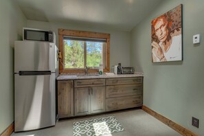 Eine Küche mit Kühlschrank, Mikrowelle, Holzschränken, einem Fenster und einem Bild an der Wand.