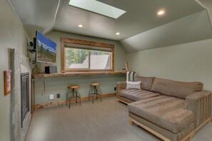 Ein gemütlicher Raum mit schrägen Wänden, einem großen Fenster, einer Couch und einem Fernseher.