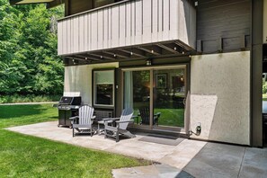 Eine Terrasse mit Grill, zwei Adirondack-Stühlen und einem Esstisch.