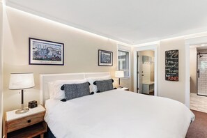 Ein Hotelzimmer mit einem großen Bett, zwei Nachttischen mit Lampen, einem gerahmten Stadtbild, einem Spiegel und einem motivierenden Zitat an der Wand.