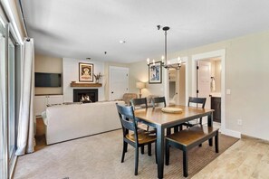 A dining area with a wooden table and chairs, a fireplace, and a chandelier. - Basecamp to All Things Northern Michigan (Boyne Falls)