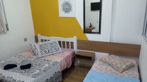 Une chambre avec deux lits, l’un recouvert d’une couvre-lit à motifs et l’autre d’une couvre-lit à fleurs. Il y a une petite table de chevet avec un miroir au-dessus.