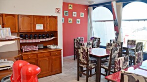 Un coin repas avec des meubles de rangement en bois, un mur rouge orné de tableaux encadrés et une fenêtre avec des rideaux.