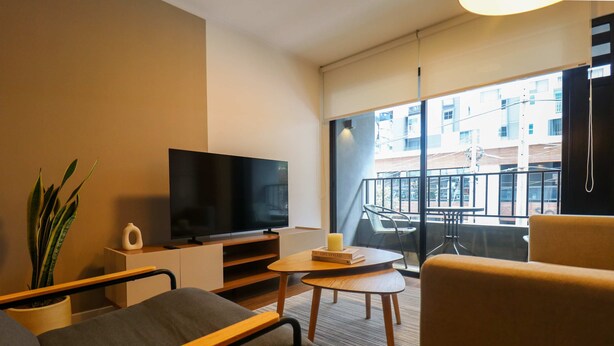 Habitació d'hotel moderna amb televisió de pantalla plana, un sofà, una taula petita, una planta en test i un balcó amb vistes a la ciutat.