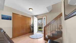 Un pasillo con puerta de madera, alfombra redonda, escalera con barandilla de madera y vista a través de un portón de cristal.