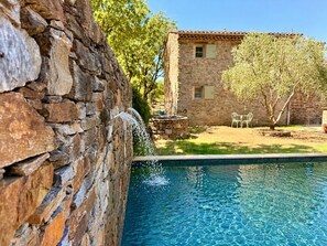 Un muro de piedra, un edificio de piedra y una piscina.