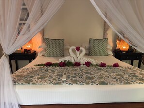 Ein Bett mit Baldachin, floraler Bettdecke, zwei Kissen und dekorativen Handtuchschwanen.
