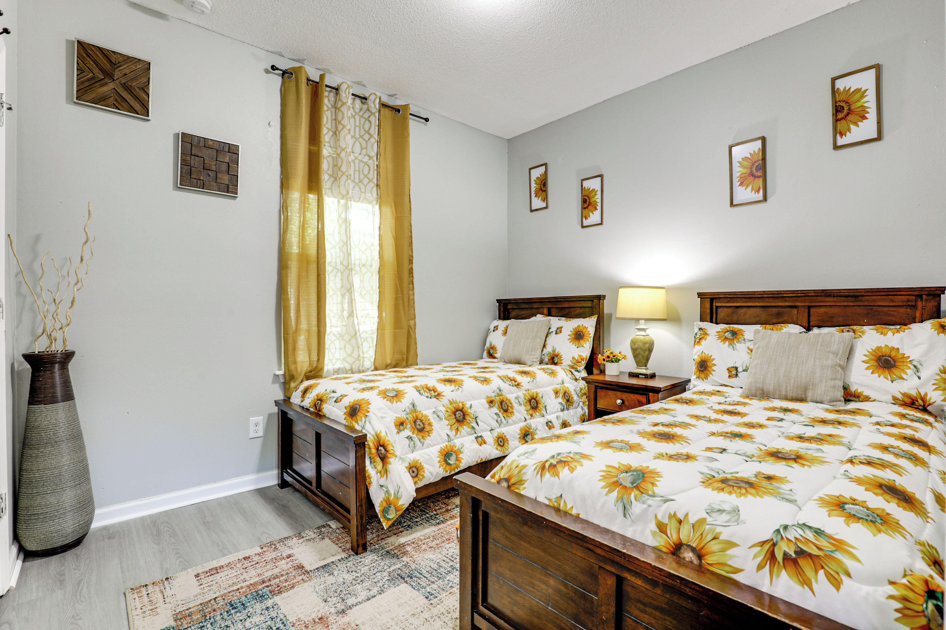 A bedroom with two beds, a nightstand, a lamp, a vase, and wall art.