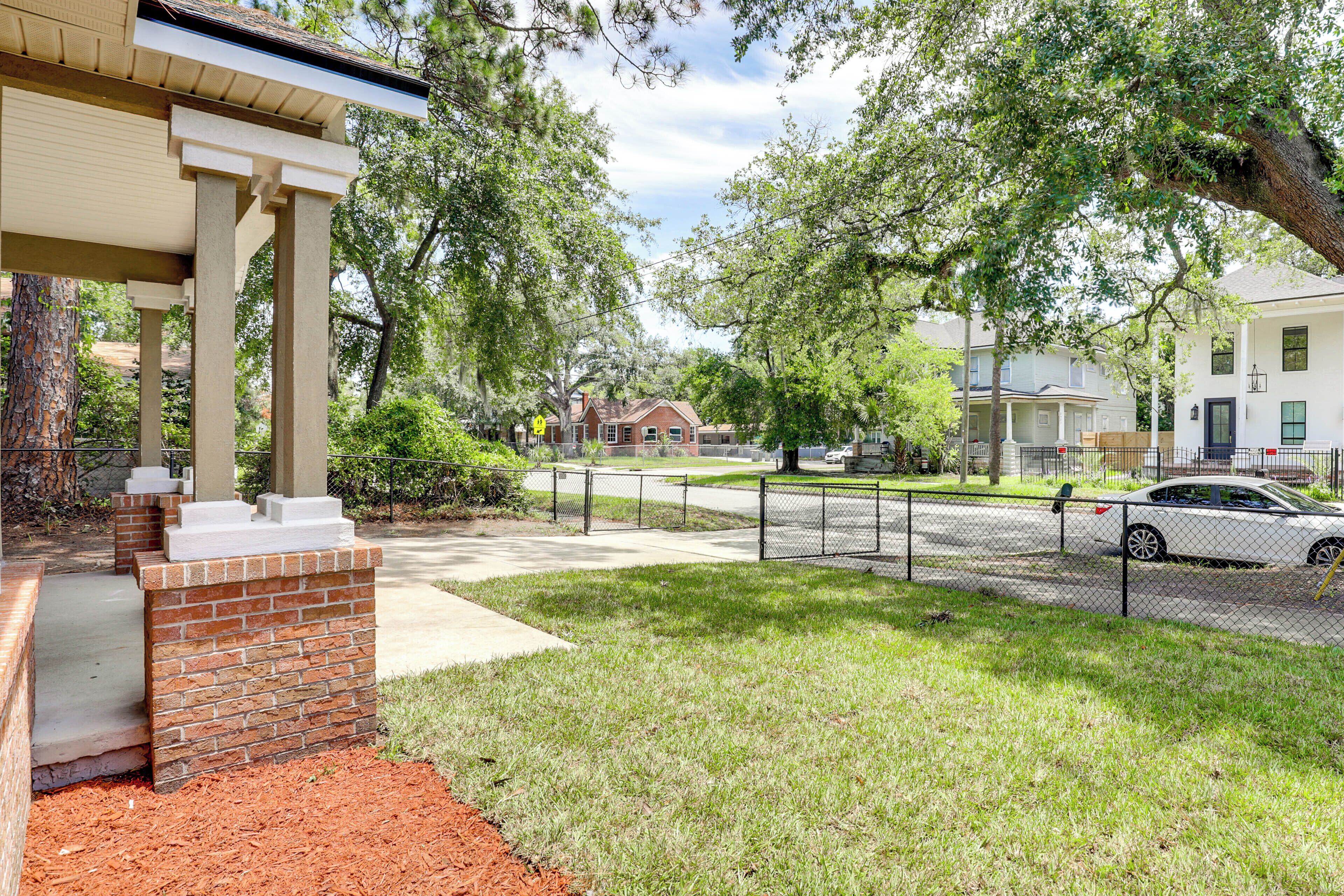 A residential area with a brick house, a covered porch, and a white car parked on the street.