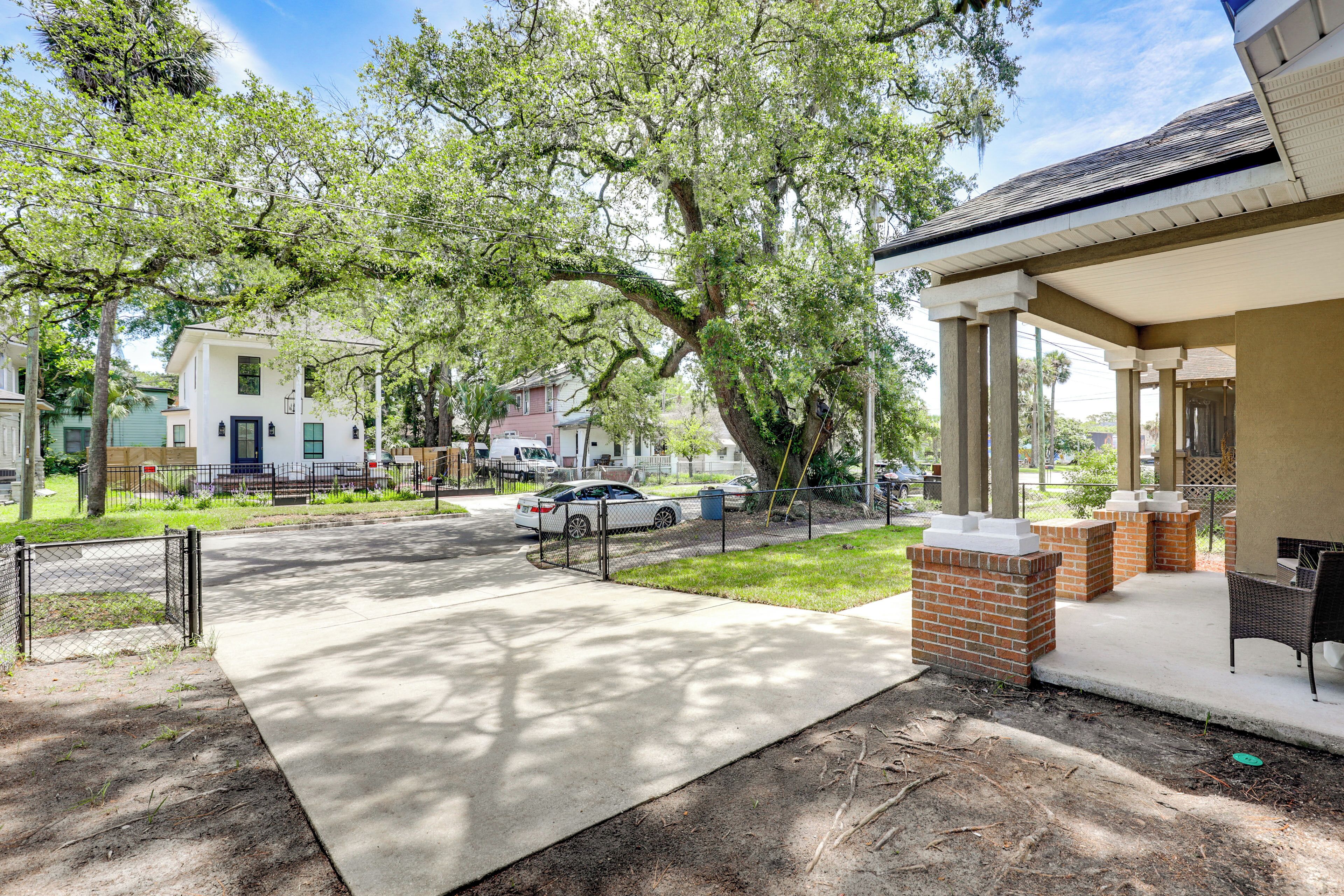 A residential area with a paved driveway, a car parked on the street, and a house with a porch.