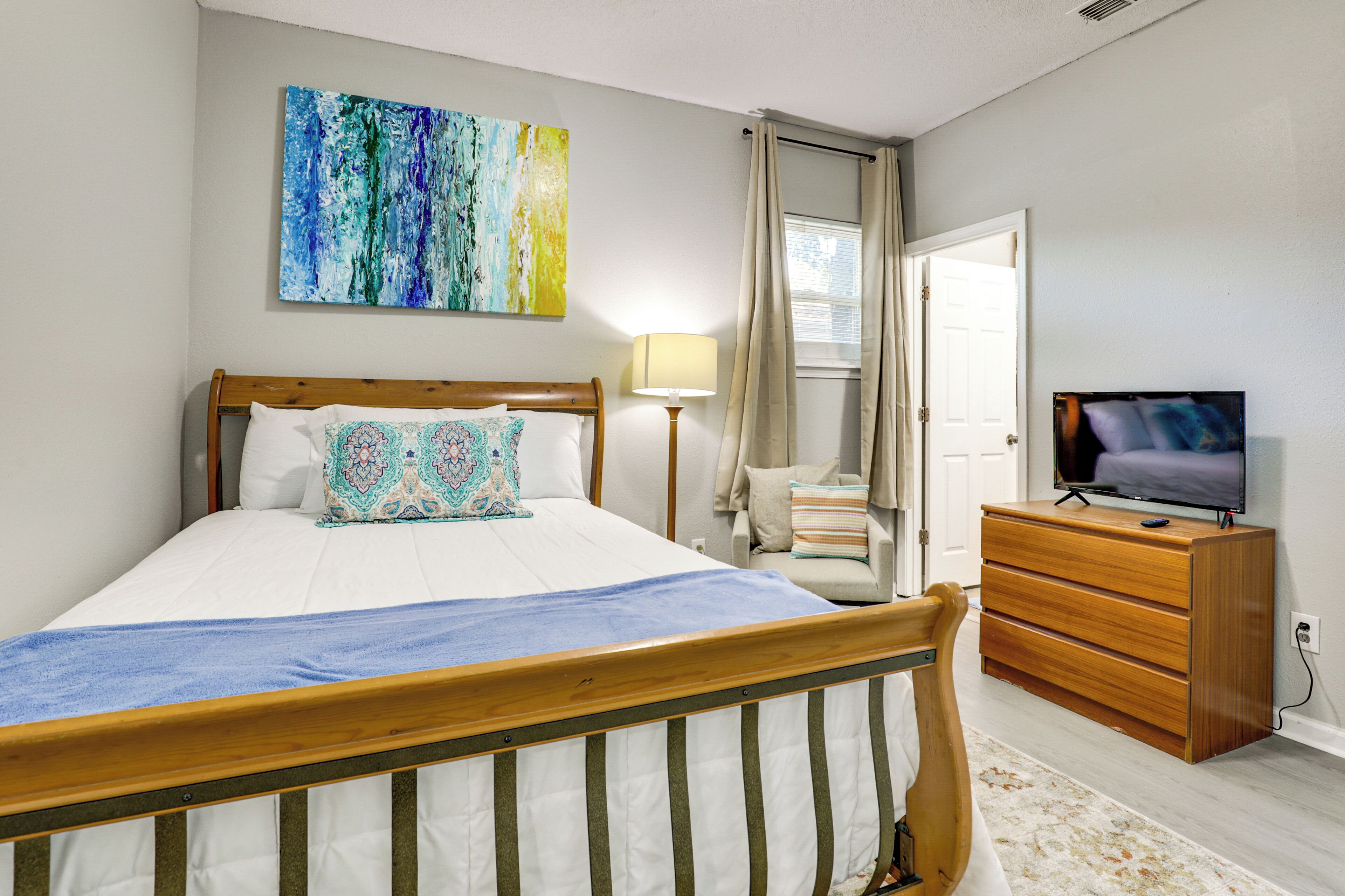 A bedroom with a bed, a dresser, a television, and a painting on the wall.