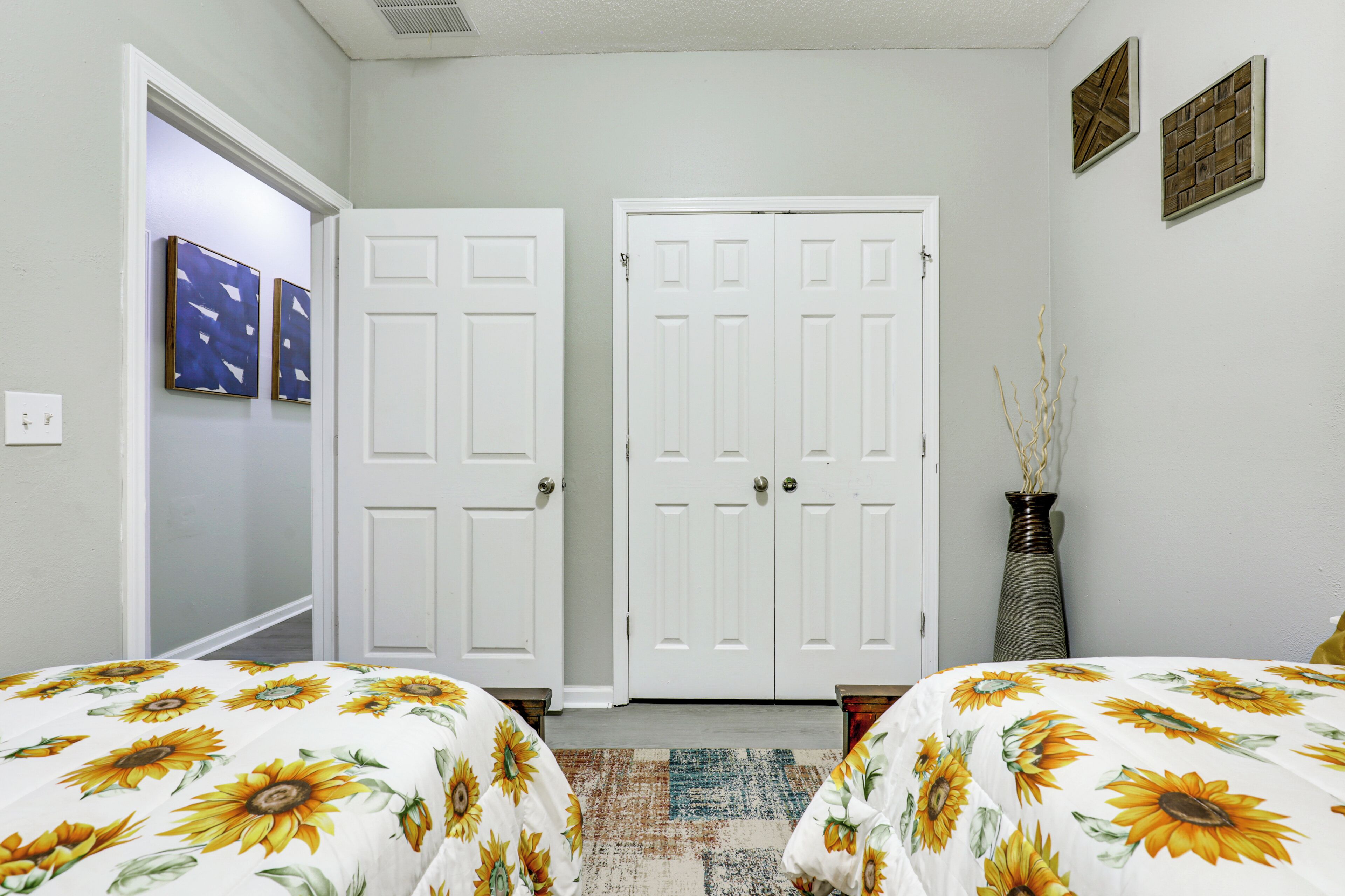 A bedroom with two beds, a door, a vase, and wall art.