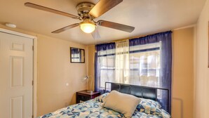 Una camera da letto con un letto, una ventola a soffitto, un comodino e una finestra con tende.