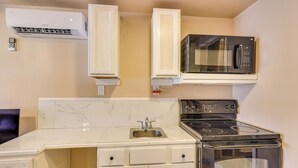Una cucina compatta con forno a microonde, piano cottura e lavello integrati, caratterizzata da mobili bianchi e piani in marmo.