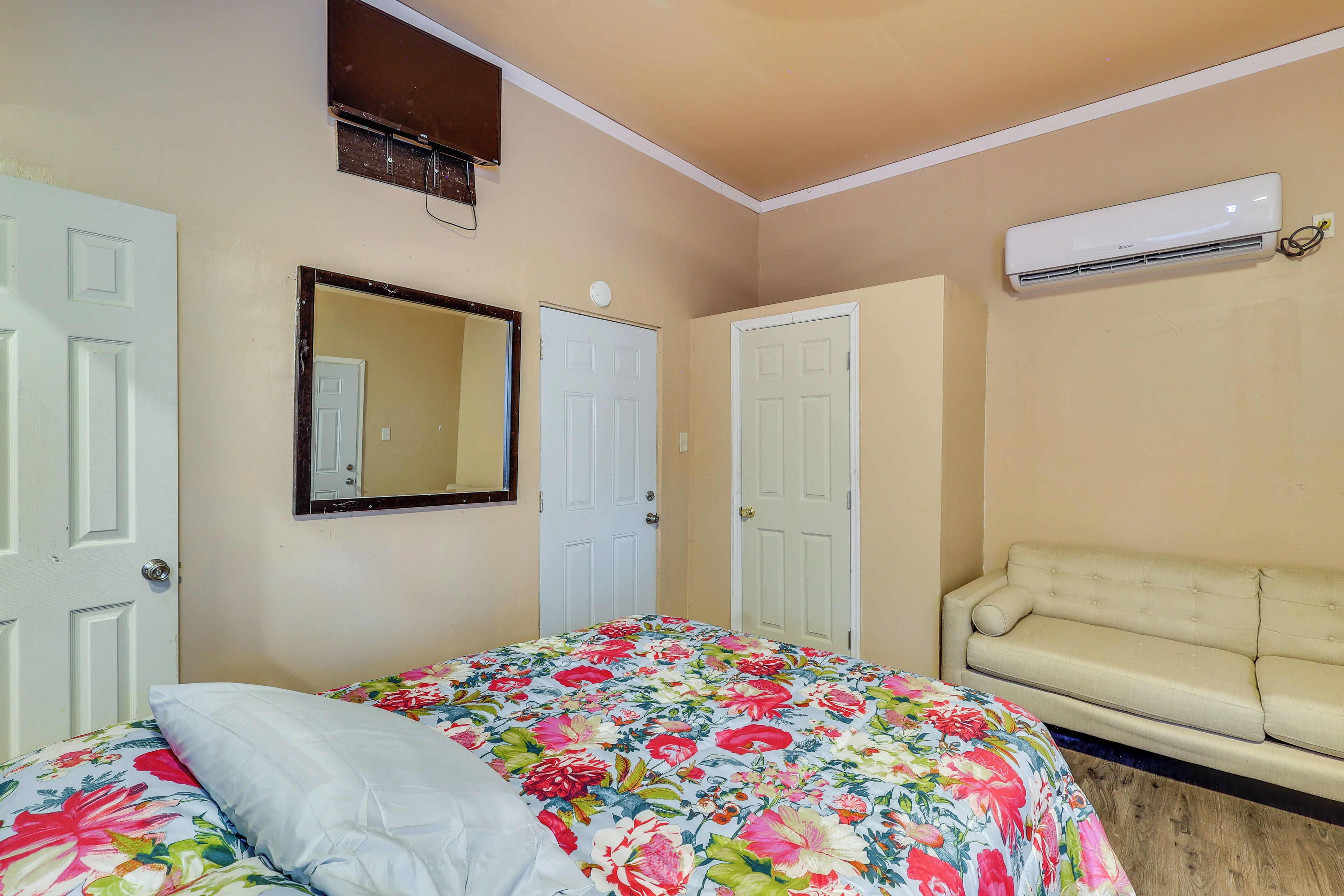 A bedroom with a floral bedspread, a beige sofa, and an air conditioning unit.