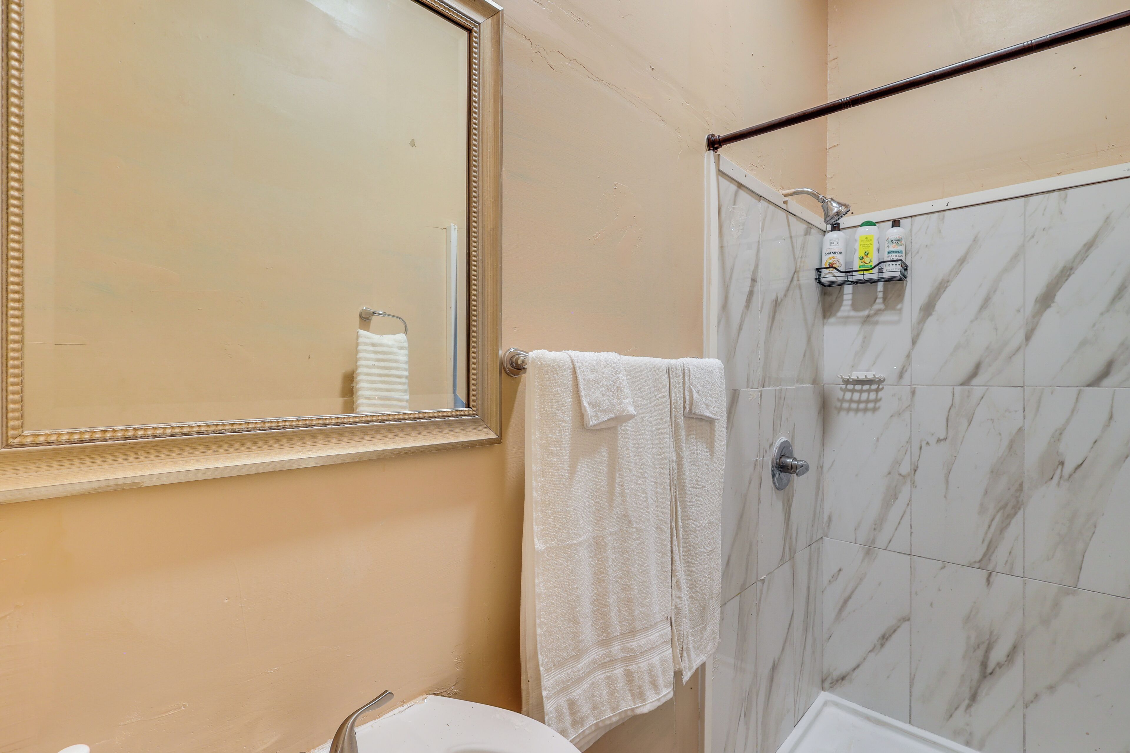 A bathroom with a marble shower, a sink, and a mirror.