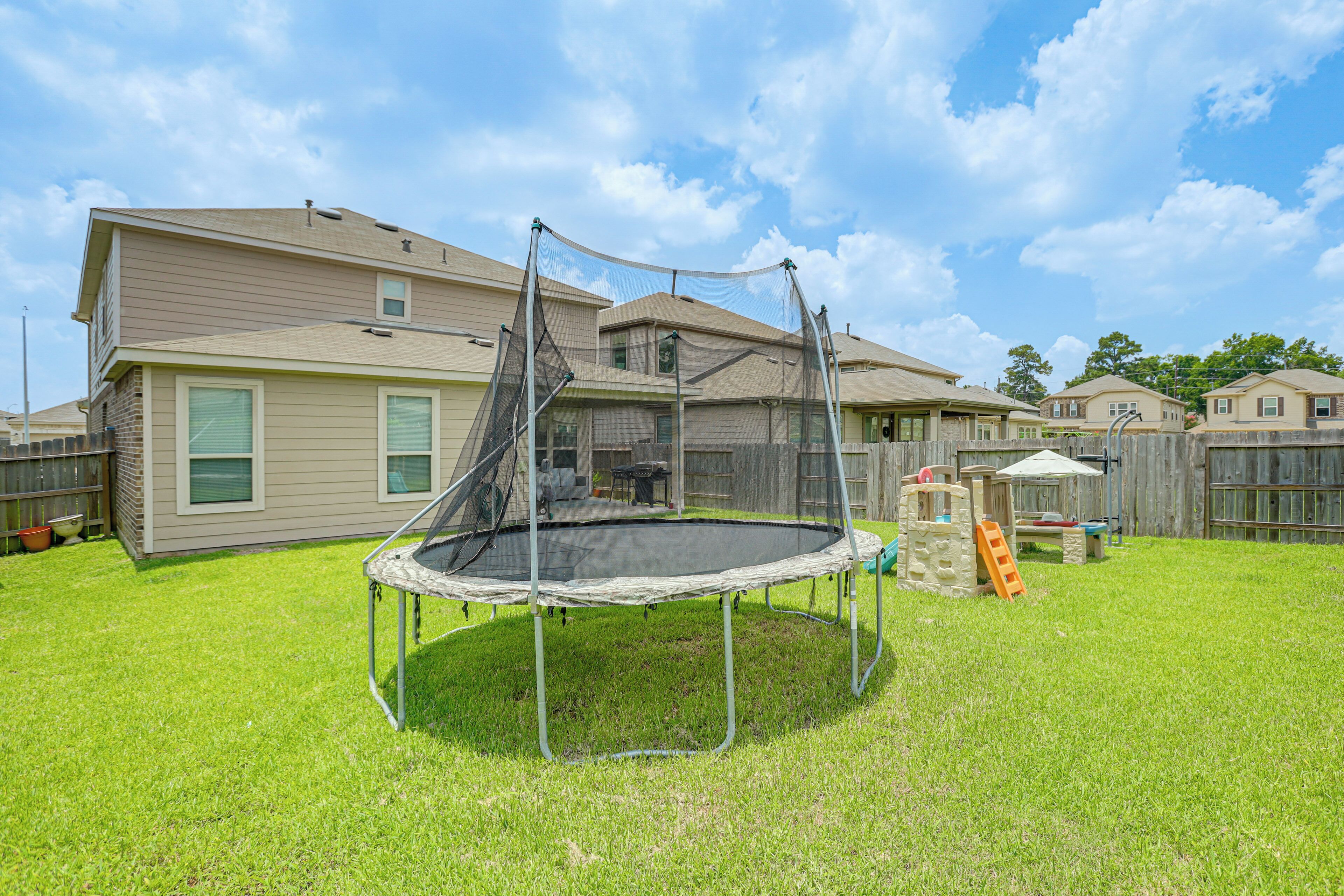A backyard with a trampoline, a wooden playhouse, and a house with beige siding.