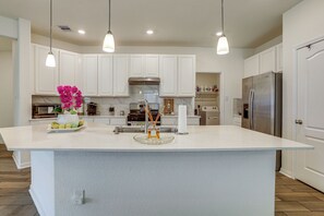 A spacious kitchen with white cabinets, a large island, stainless steel appliances, pendant lighting, and a marble backsplash.