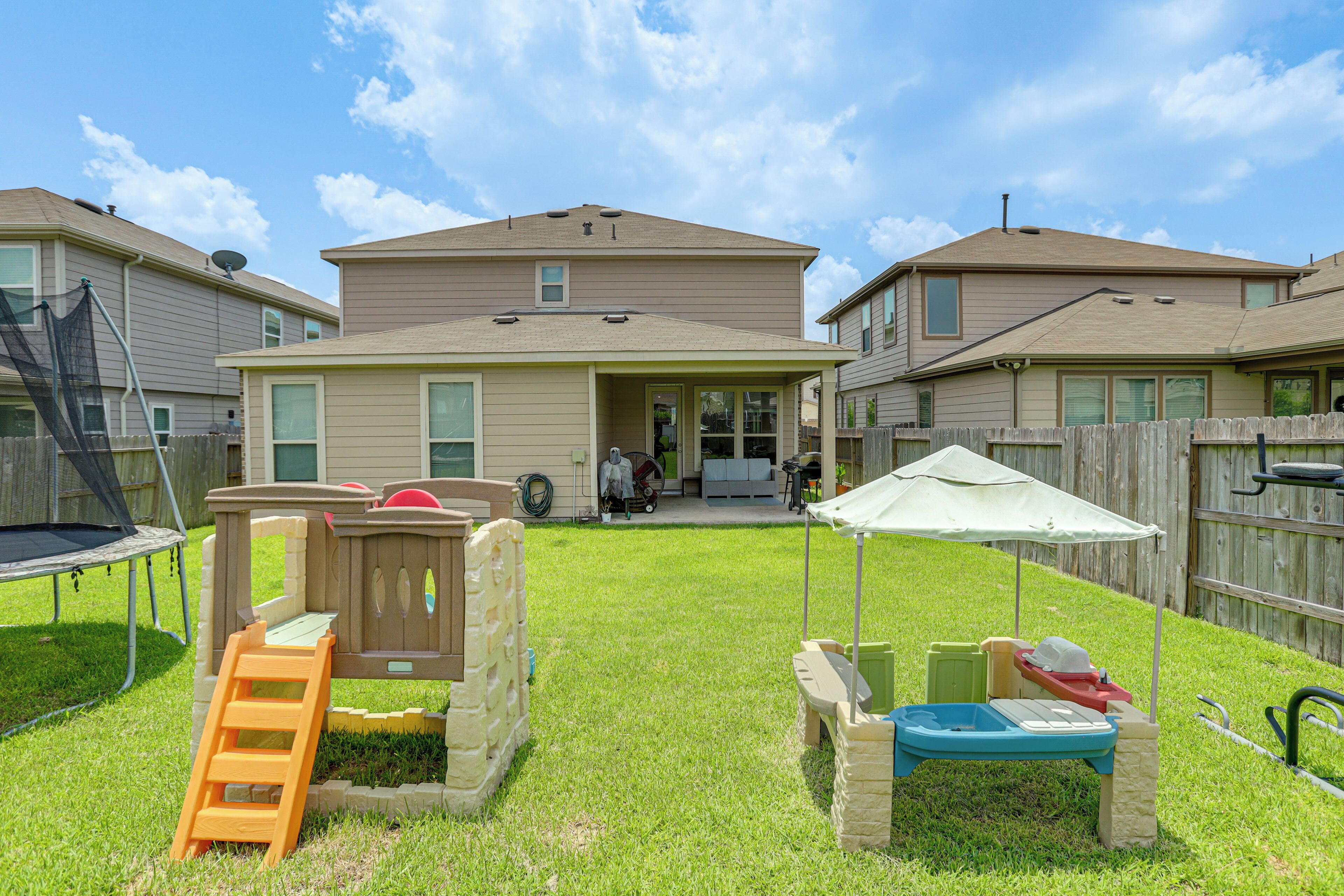 A residential backyard with a play structure, a trampoline, and a wooden fence.