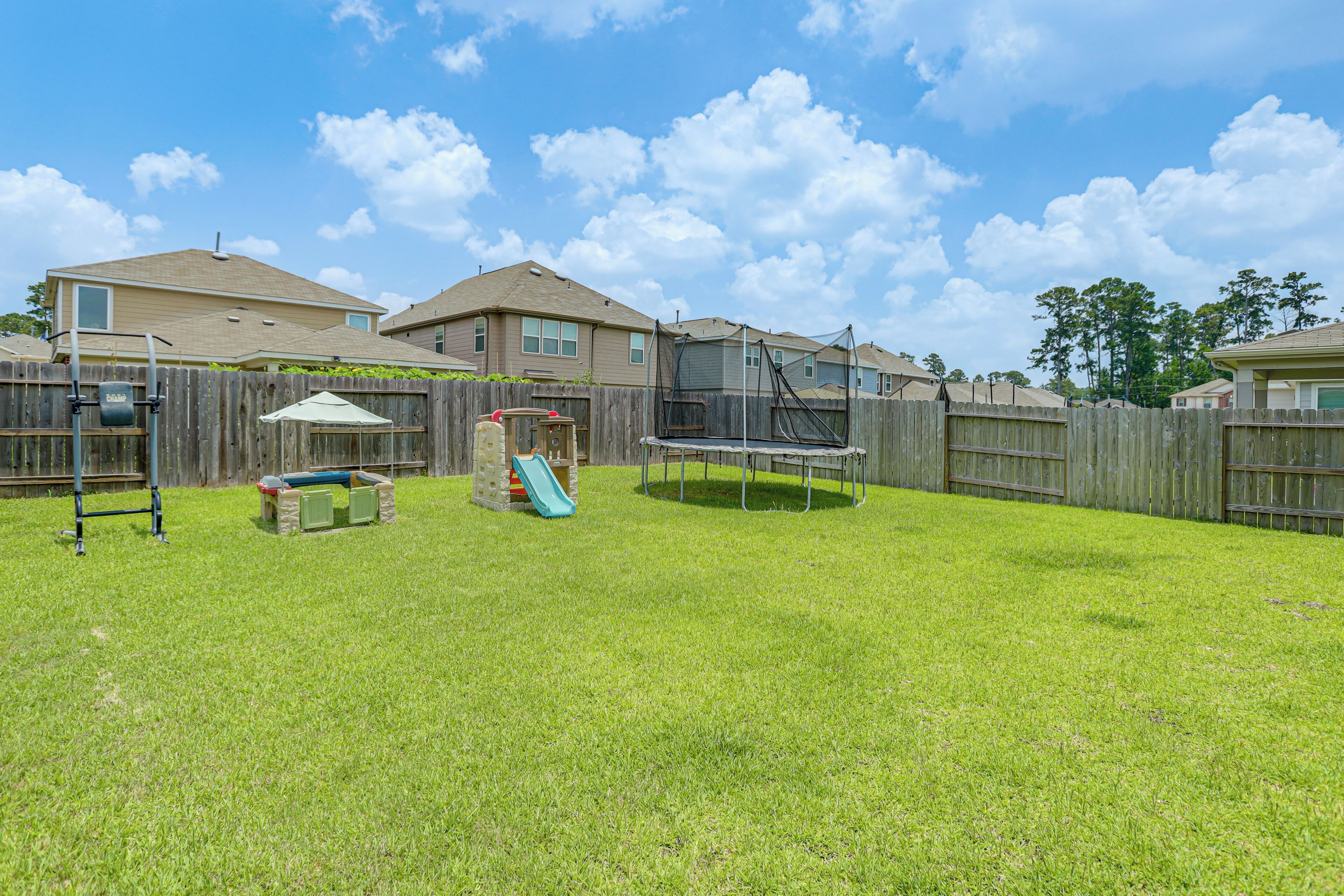 A backyard with a trampoline, a slide, and a wooden fence.