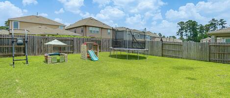 A backyard with a trampoline, a slide, and a wooden fence.