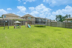 A backyard with a trampoline, a slide, and a wooden fence.