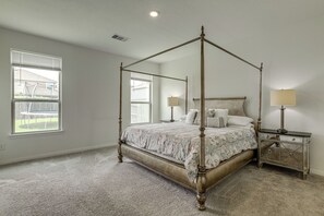 A four-poster bed with a floral bedspread, two bedside tables with lamps, and a large window with blinds.