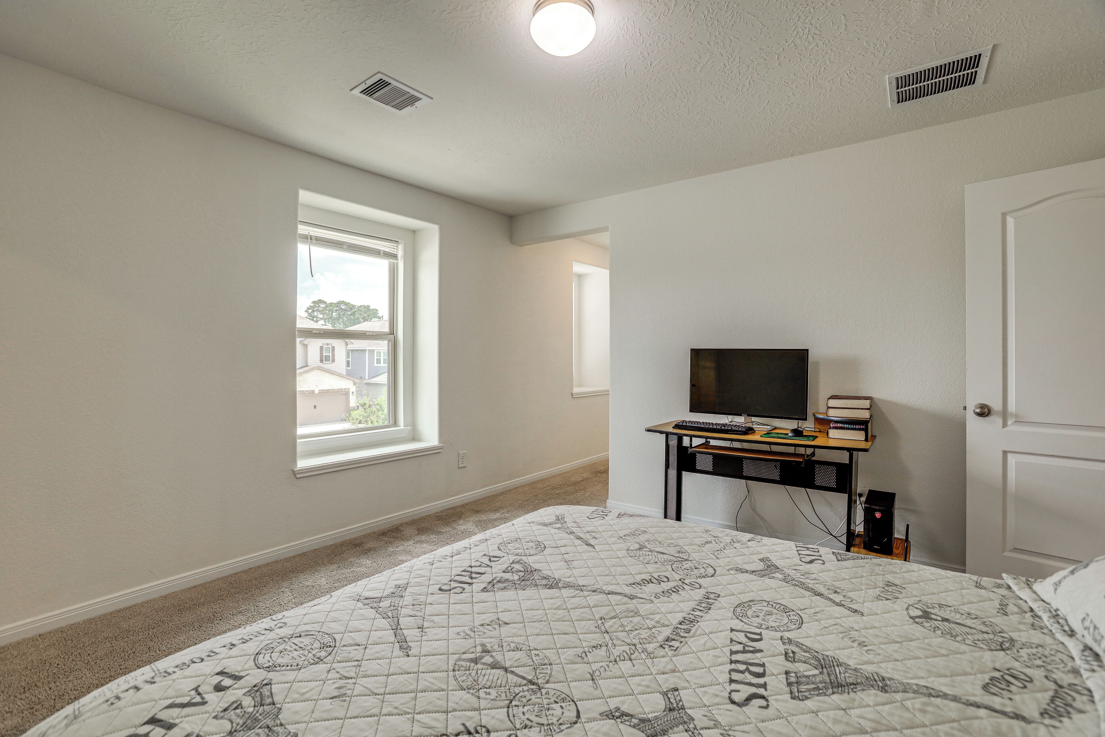 A bedroom with a bed, a desk with a computer, a window, and a door.